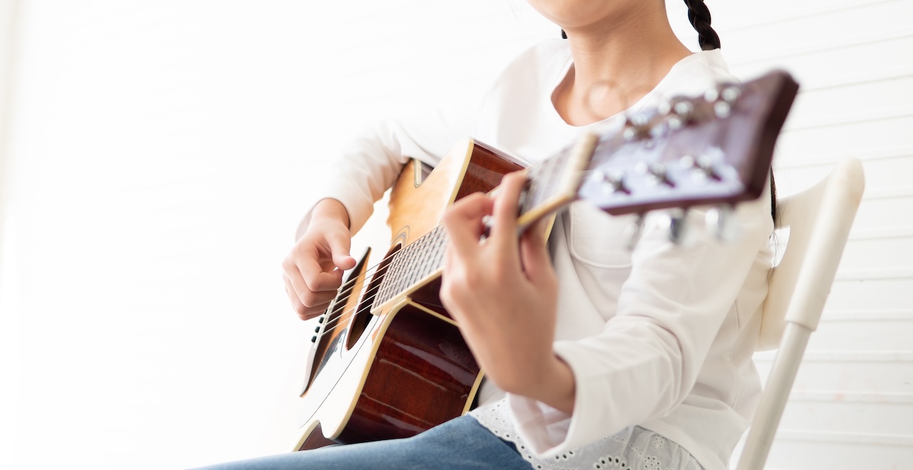 Young girl musician holds wooden acoustic guitar neck and fingerpicking melody.